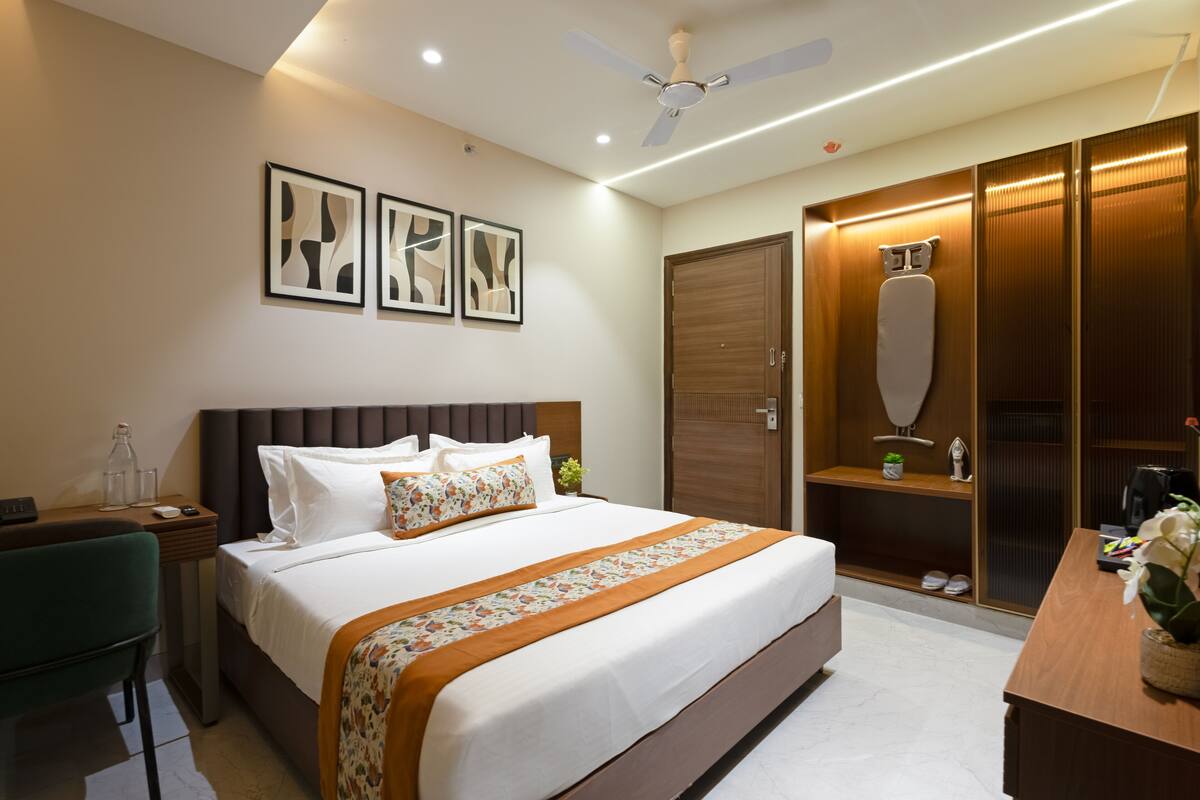 Une chambre d’hôtel avec un grand lit, un bureau avec une chaise, une armoire et un ventilateur de plafond.