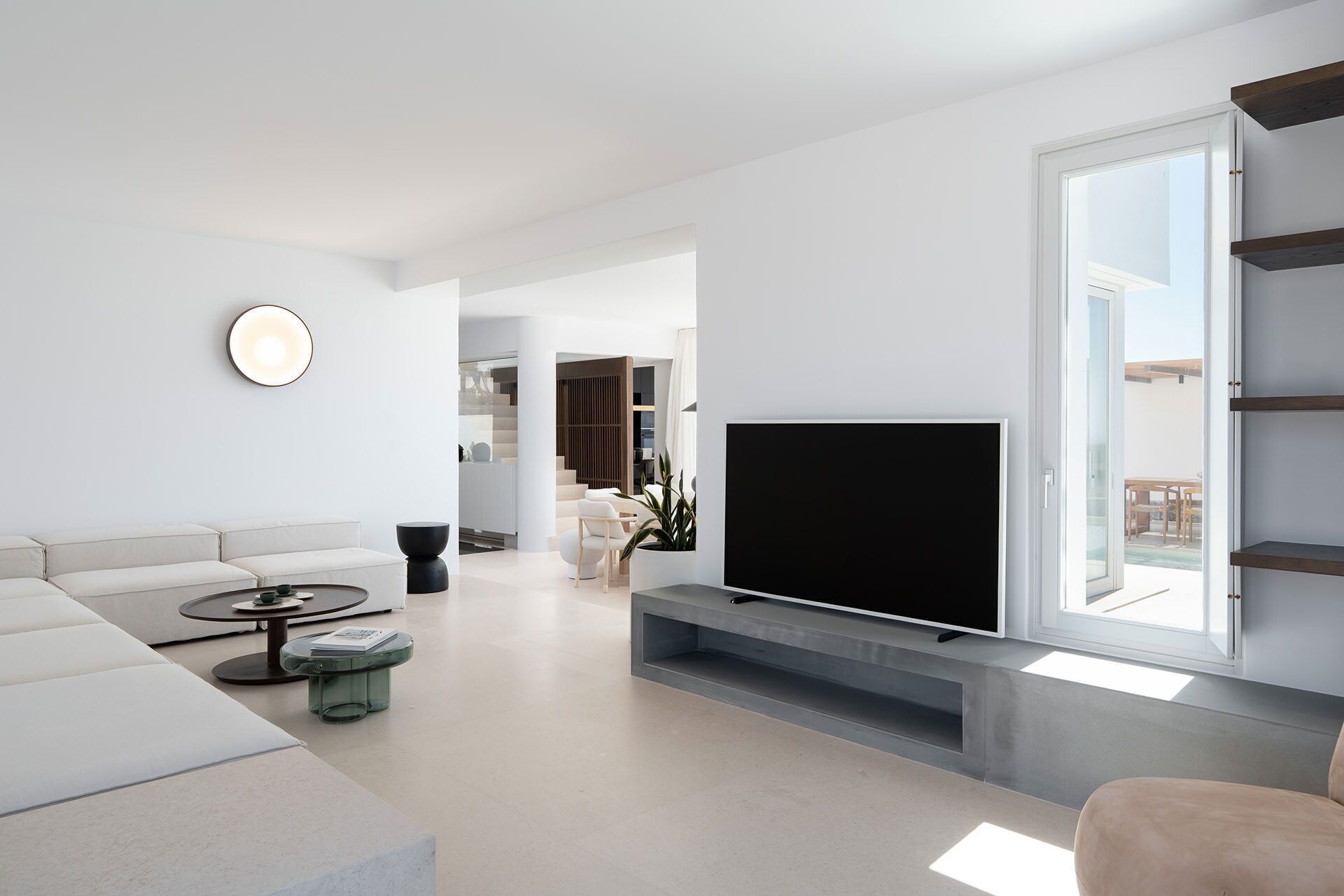 A modern living room with a large flat-screen TV, a sofa, a coffee table, and a dining area visible through an open door.