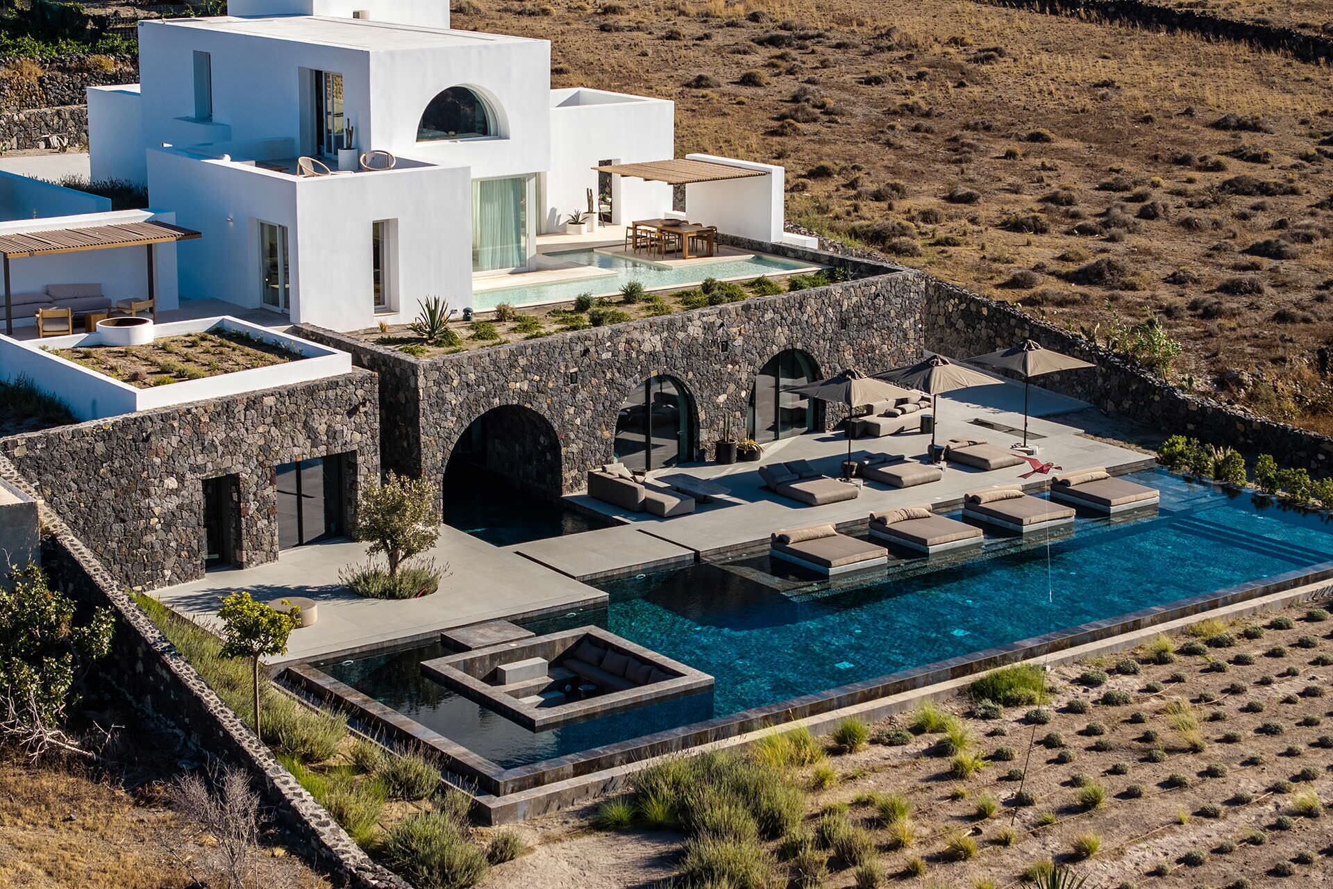 A modern villa with a swimming pool, stone walls, and outdoor seating areas.