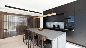 A modern kitchen with a central island, dark cabinetry, and a view through the window. - Villa Kallisti with private pool - My Rental Homes (Ia)