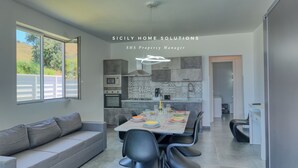 Una cocina moderna con comedor, que incluye un sofá gris, mesa de comedor con sillas y vistas al exterior.