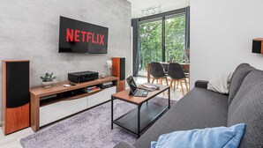Ein modernes Wohnzimmer mit einem an der Wand befestigten Flachbildfernseher, einer Holz-Unterhaltungseinheit, einem grauen Sofa und einem Essbereich mit einem Balkon.