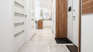 Ein moderner Flur mit weißen Türen, einer Wand als Holzdekor und einem Küchenbereich im Hintergrund.