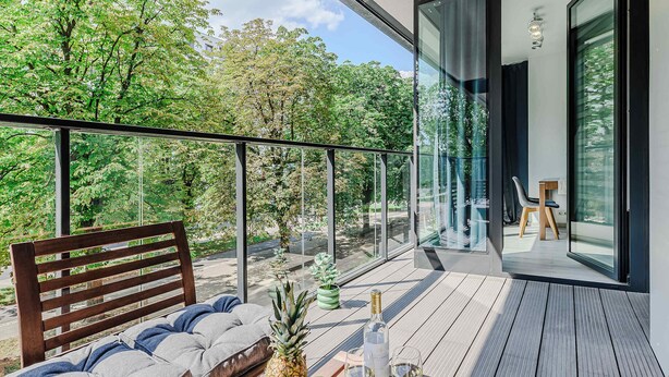 Ein Balkon mit einer hölzernen Sitzbank, einer Obstschale und einer Weinflasche.