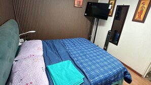 Een hotelkamer met een bed, een flatscreen televisie aan de muur en een raam met jaloezieën.