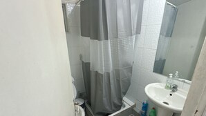 Een badkamer met douche, toilet, wastafel en spiegel.