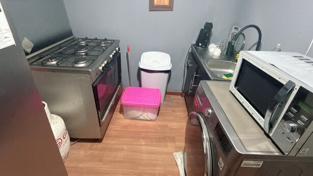 Een compacte keuken met een gasfornuis, oven, magnetron en een spoelbak.