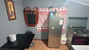 Een kleine keuken met een koelkast, fornuis en een tafel met een stoel.