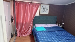 Een slaapkamer met een bed, een ventilator, een gordijn en een ingelijste foto aan de muur.