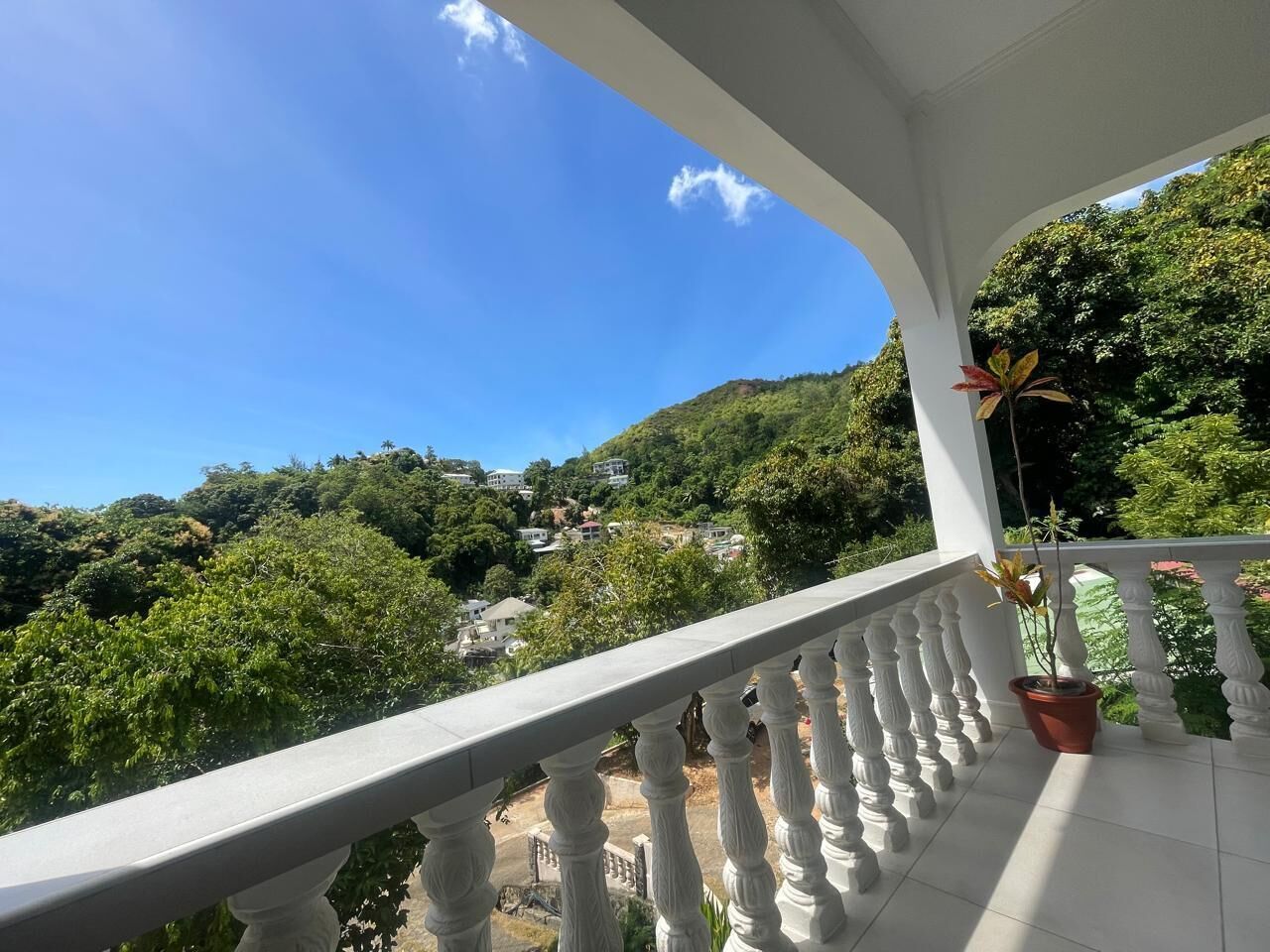 A balcony with a white balustrade overlooking a hillside with greenery and houses.