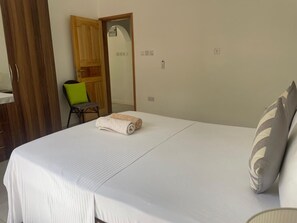A hotel room with a bed, a chair, a wooden wardrobe, and a door.