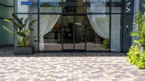 A hotel entrance with glass doors, a blue sign indicating the entrance, and a tiled pavement.
