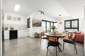Une cuisine moderne avec des meubles blancs, un lave-vaisselle noir et un coin repas comprenant une table ronde et des chaises.