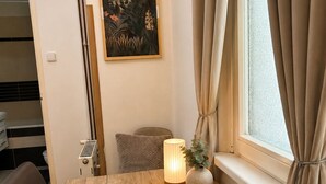 Ein Zimmer mit einem Holztisch, einem Wandbild, einem Fenster mit Vorhängen und einer Nachttischlampe.