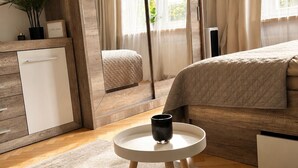 Ein modernes Schlafzimmer mit Bett, Nachttisch mit Tasse, Kleiderschrank, Spiegel und einer Topfpflanze.