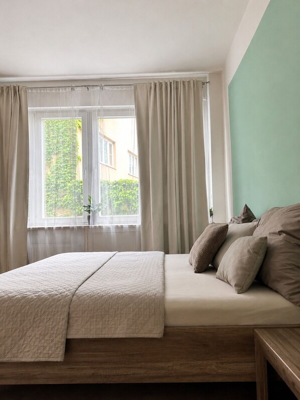 Une chambre à coucher avec un lit, une fenêtre avec des rideaux et une vue sur la verdure à l’extérieur.