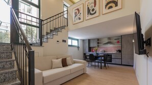 A modern living room with a staircase, a sofa, and a kitchen area in the background. - Lofts Cit Turin by Wonderful Italy (Turin)