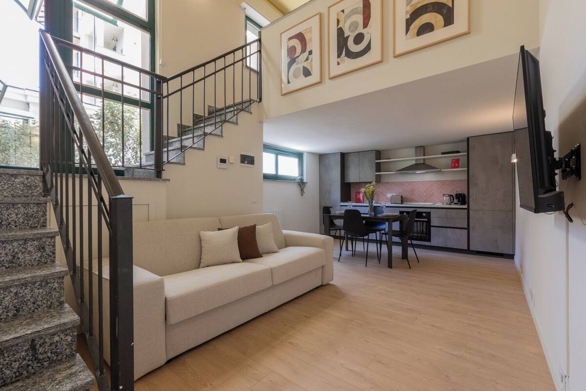 A modern living room with a staircase, a sofa, and a kitchen area in the background.