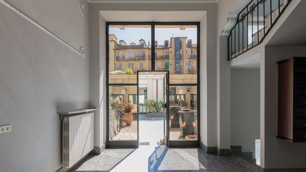 A hallway with a glass door leading to an outdoor area with potted plants and a bicycle. - Lofts Cit Turin by Wonderful Italy (Turin)