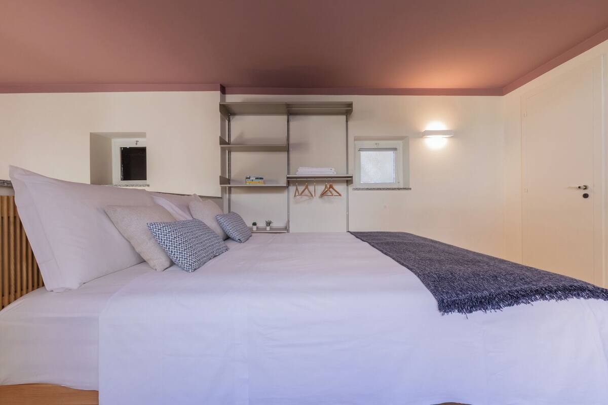 A bedroom with a bed, a wardrobe, a shelf unit, and a small window.