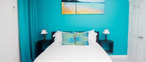 A bedroom with a large bed, teal walls, and a painting above the bed.