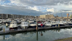 Un puerto deportivo con numerosas embarcaciones amarradas, un paseo marítimo y edificios residenciales al fondo.