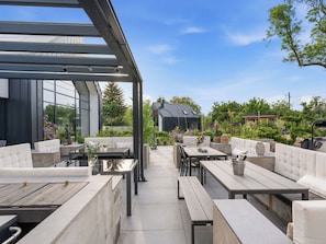 An outdoor patio with modern furniture, a glass enclosure, and a view of a house in the background.
