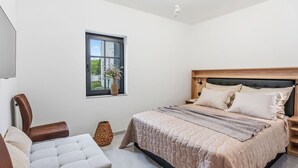 Et soveværelse med seng, sengeborde, en stol, et vindue og en loftlampe.