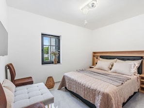 A bedroom with a bed, bedside tables, a chair, a window, and a ceiling light fixture.