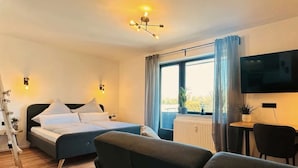 Una habitación de hotel moderna con cama, escritorio, silla, televisor y un amplio ventanal con cortinas.