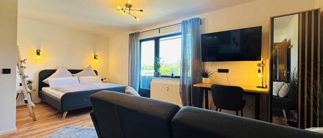 Quarto de hotel moderno com cama, sofá, escrivaninha e televisão.
