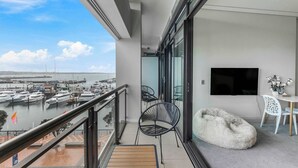 A balcony with a view of a marina, a white bean bag chair, a small table with two chairs, and a flat-screen TV on the wall. - Comfort, Harbour Views & Balcony | Zodiak Stays (Auckland)