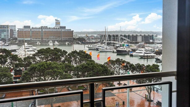 A marina with boats, a large building with a flag, and a clear sky. - Comfort, Harbour Views & Balcony | Zodiak Stays (Auckland)