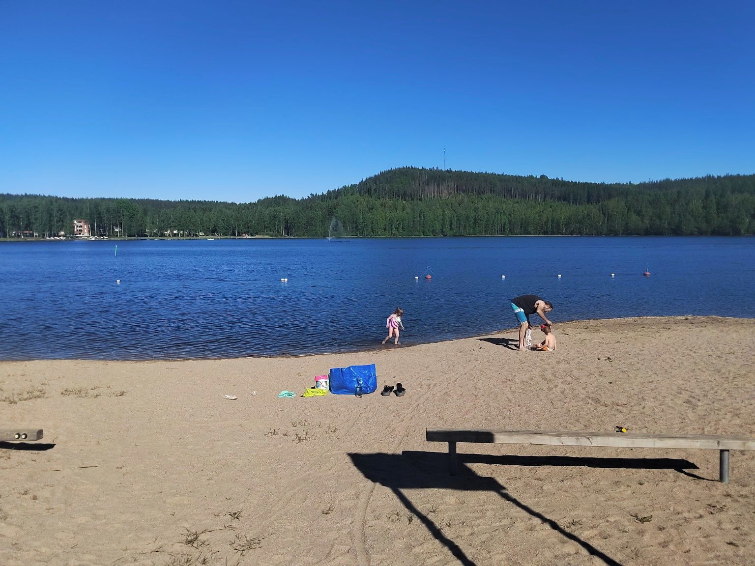 A sandy beach with a wooden bench, a child, and an adult.