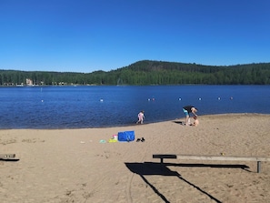 A sandy beach with a wooden bench, a child, and an adult. - Riverfront Cottage and Sauna (Äänekoski)