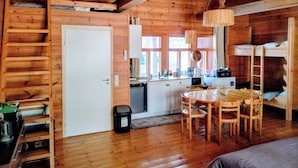A wooden cabin interior with a dining area, kitchen, bunk beds, and a door. - Riverfront Cottageee (Äänekoski)