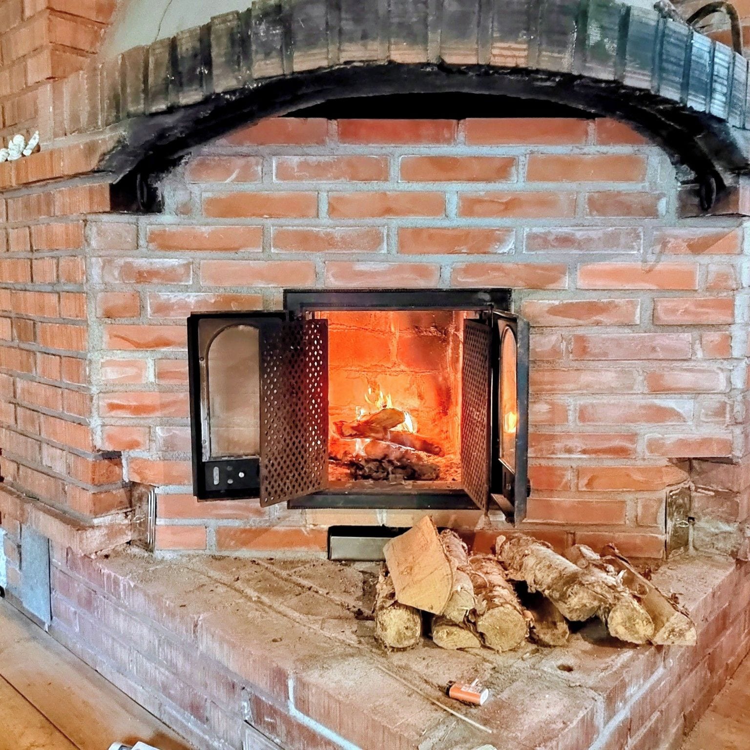 Una llar de totx amb foc encès a dins, llenya col·locada al davant i una reixeta metàl·lica.