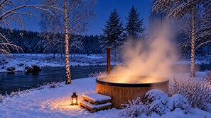 A wooden hot tub surrounded by snow-covered trees and a river. - Riverfront Cottage and Sauna (Äänekoski)