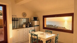 A kitchen with a dining table and chairs, a view of the sea through a window, and a clock on the wall.
