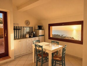 Une cuisine avec une table et des chaises, une vue sur la mer par la fenêtre et une horloge au mur.