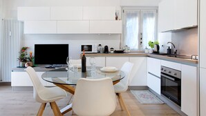 Une cuisine moderne avec un coin repas, des meubles blancs, un téléviseur à écran plat et un four encastré.