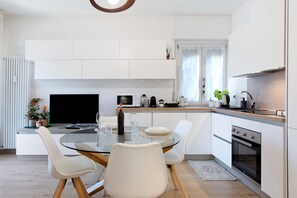 A modern kitchen with a dining area, white cabinetry, a flat-screen TV, and a built-in oven. - Apartment 'Emmie House' with Mountain View, Balcony and Wi-Fi (Aosta)