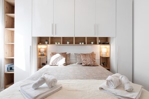 A hotel room with a bed, two bedside tables, a nightstand, a wardrobe, and built-in shelves with decorative items. - Apartment 'Emmie House' with Mountain View, Balcony and Wi-Fi (Aosta)