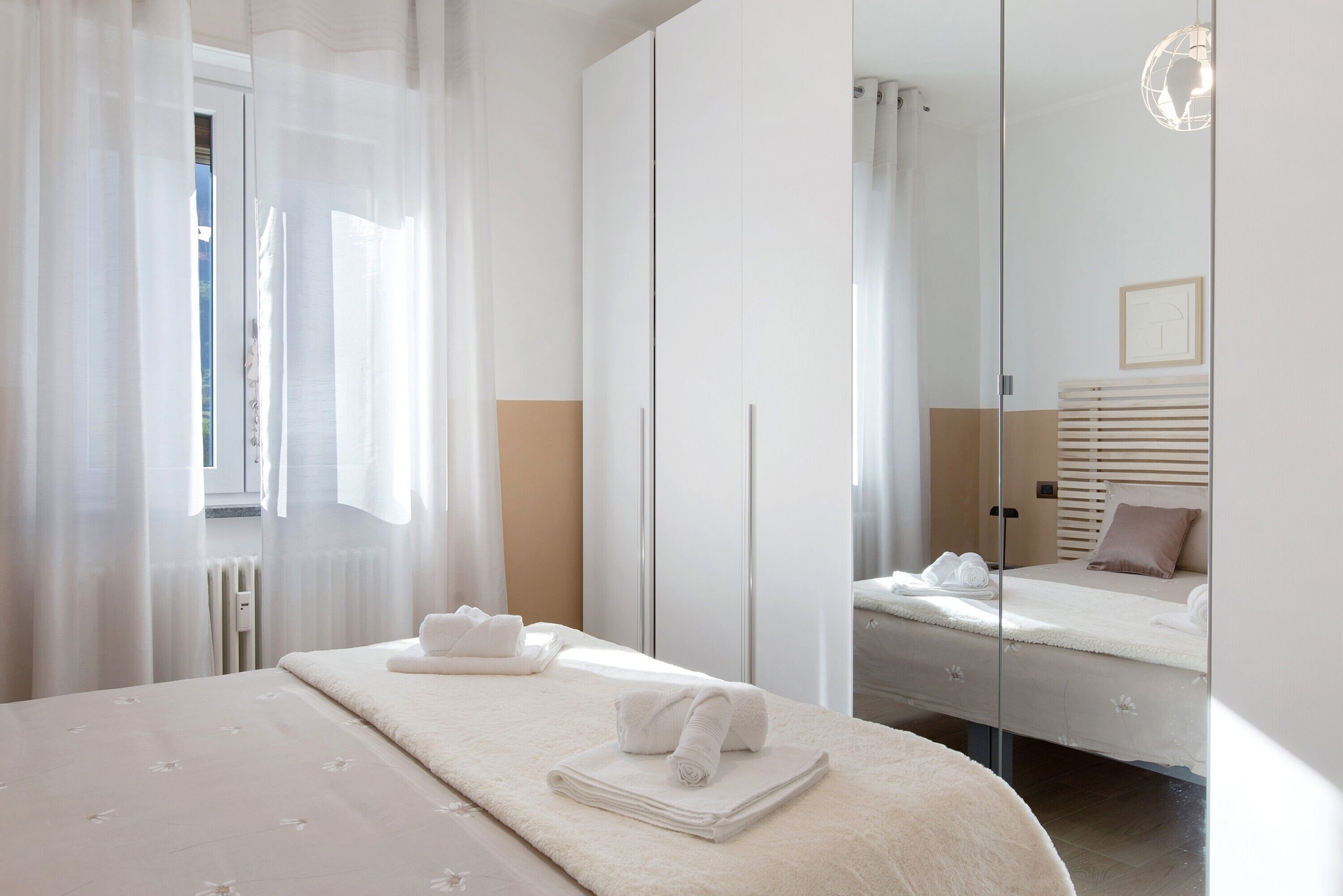 A hotel room with a bed, a large mirror, and a window with sheer curtains.