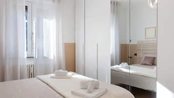 A hotel room with a bed, a large mirror, and a window with sheer curtains.