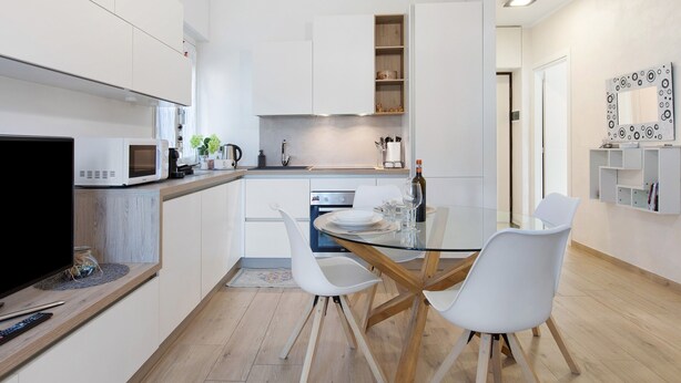 Une cuisine moderne avec des meubles blancs, une table à manger en verre et un téléviseur à écran plat.