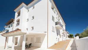 A white multi-story building with balconies and a covered outdoor seating area. - Charming Baia Marina apartment (Orosei)