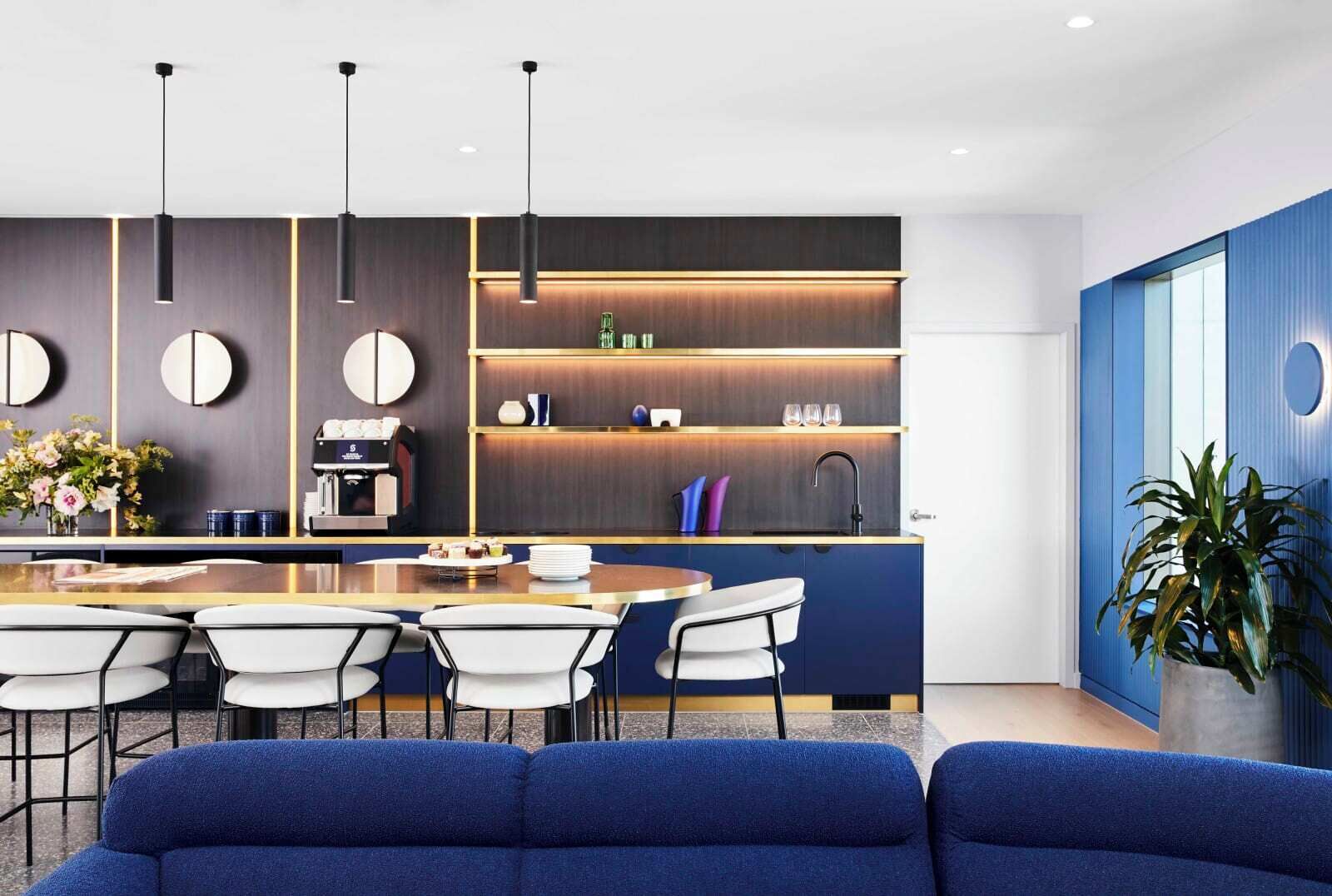 Een moderne keuken met een centraal eiland, barstoelen en een zithoek met een blauwe bank.