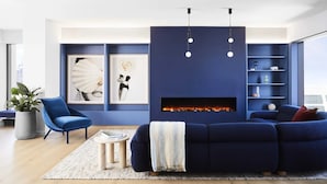 A modern living room with a blue sofa, a blue armchair, a fireplace, and a bookshelf.