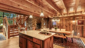 A rustic interior with a stone fireplace, wooden beams, a dining area, and a staircase.